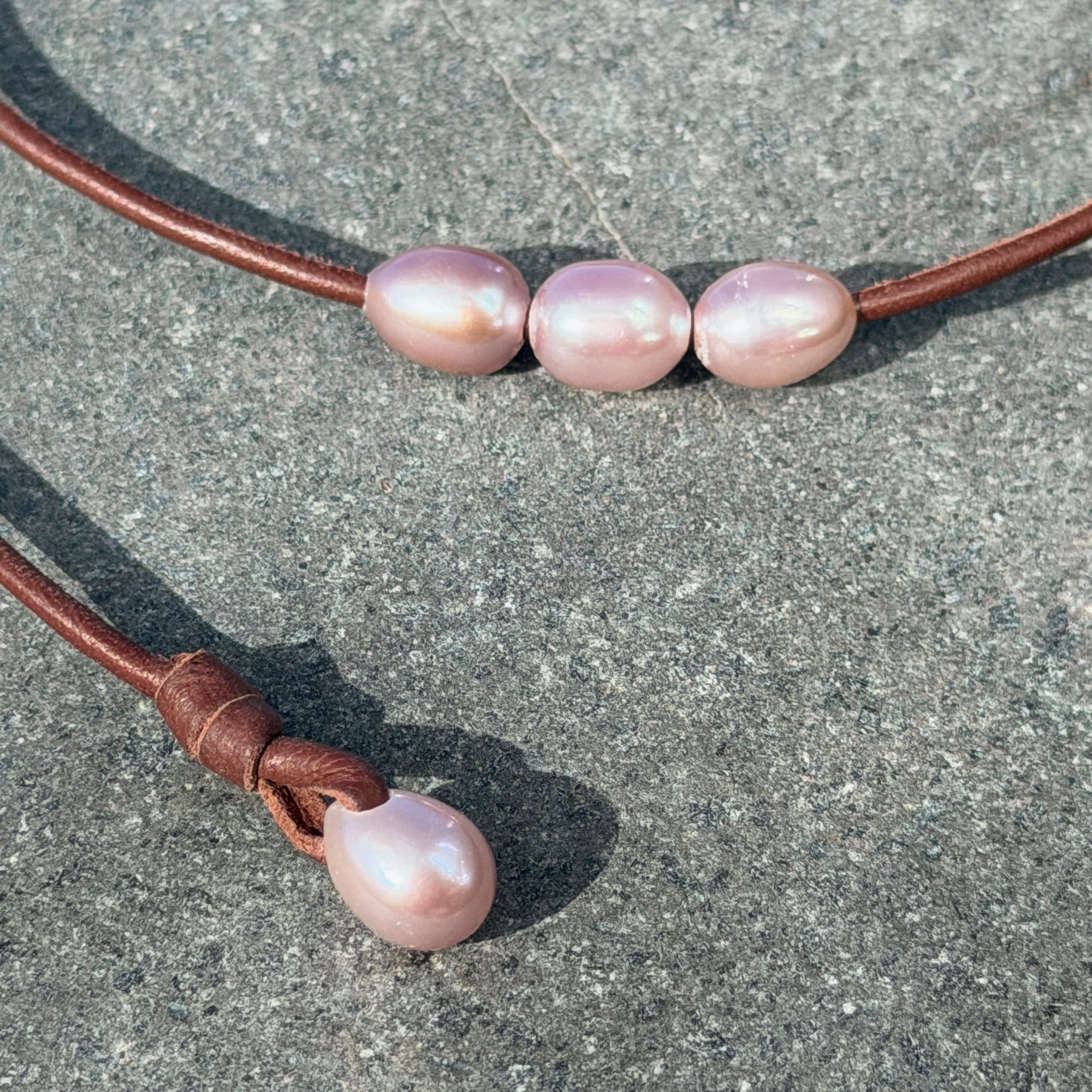 Ras du cou en cuir et trois perles roses ovales, sur une pierre, détail.