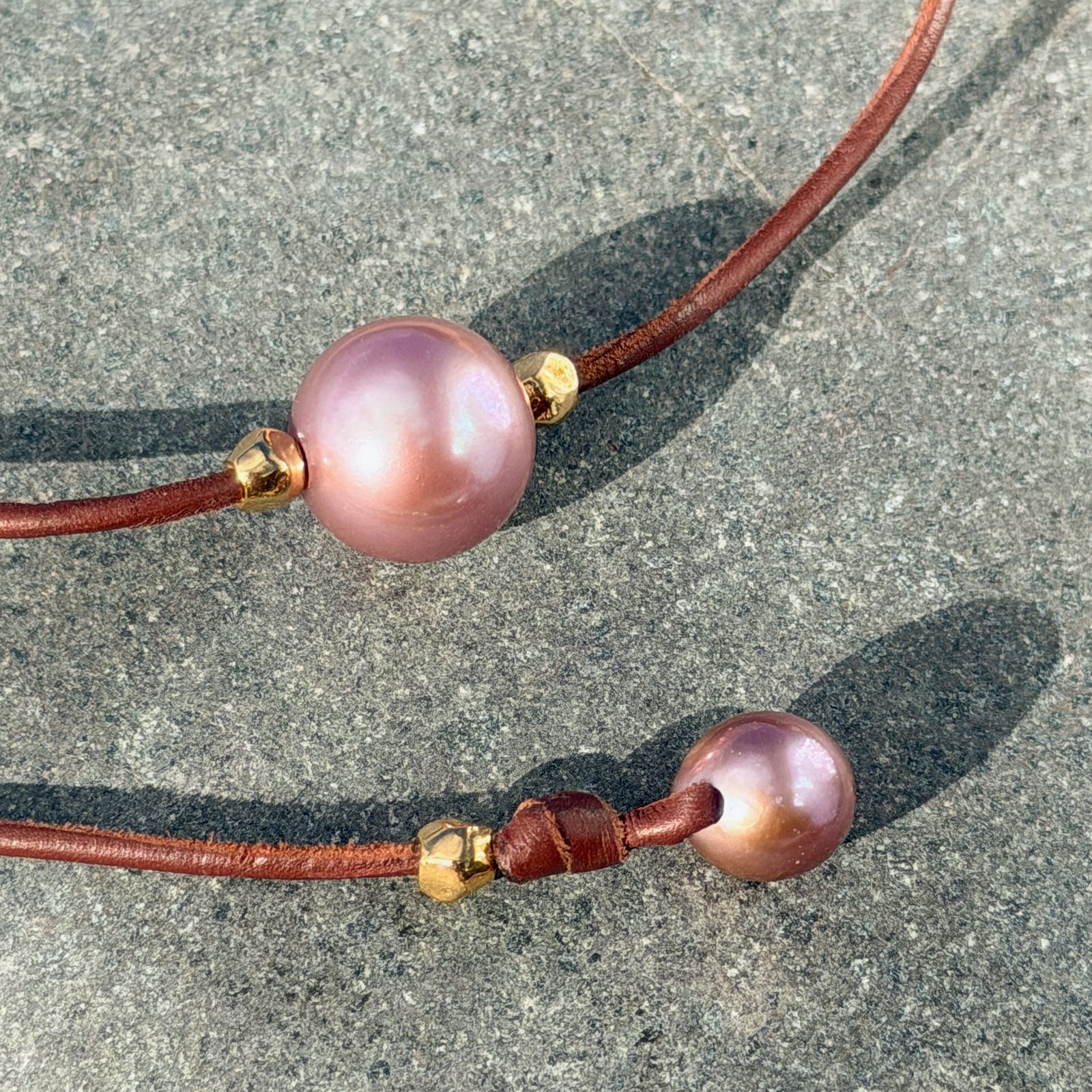 Ras du cou en cuir, perle rose et billes en plaqué or, sur une pierre, détail.