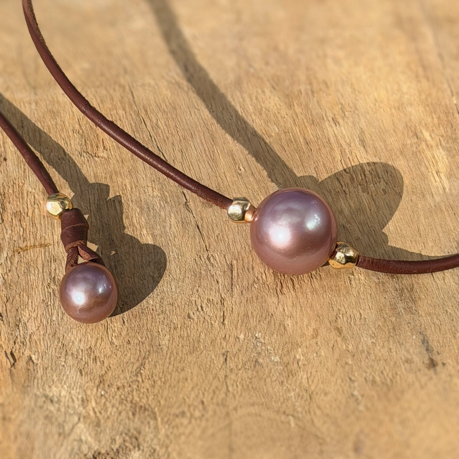 Ras du cou en cuir, perle rose et billes en plaqué or, sur du bois, détail.