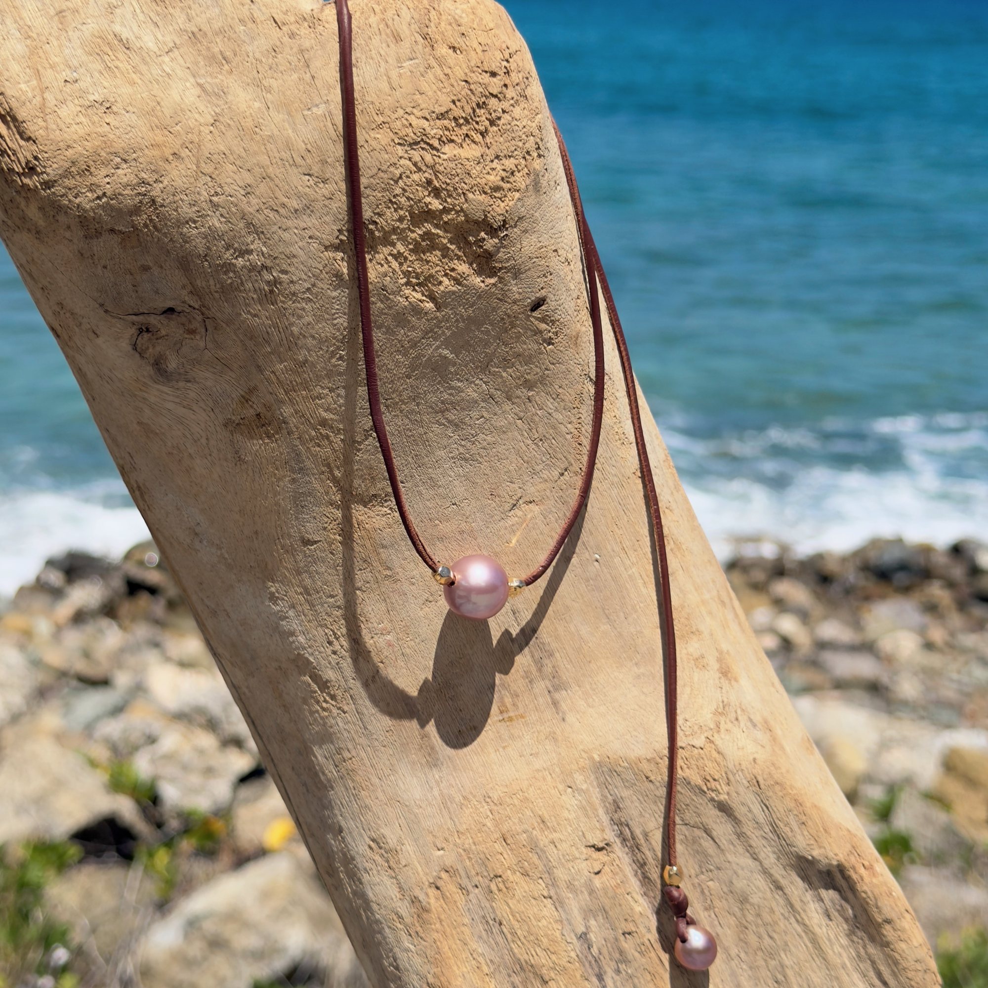 Ras du cou en cuir, perle rose et billes en plaqué or, sur du bois.