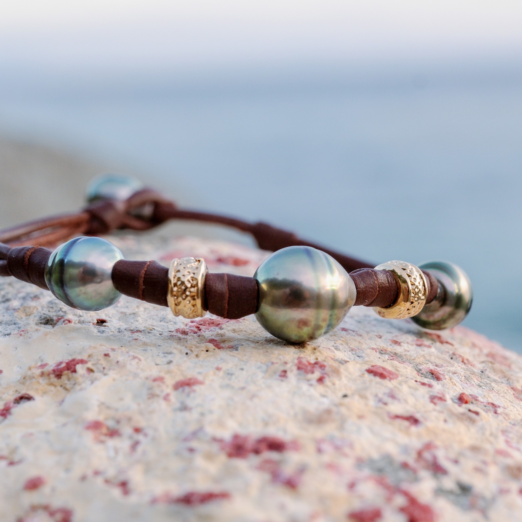 Bracelet en cuir, trois perles baroques de Tahiti et rondelles dorées, sur une pierre, détail.