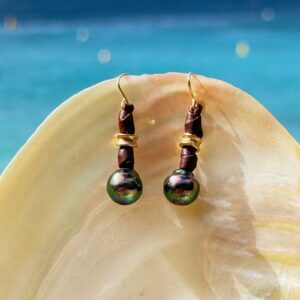 Boucles en cuir, perles vertes de Tahiti et crochets en or, sur un coquillage.