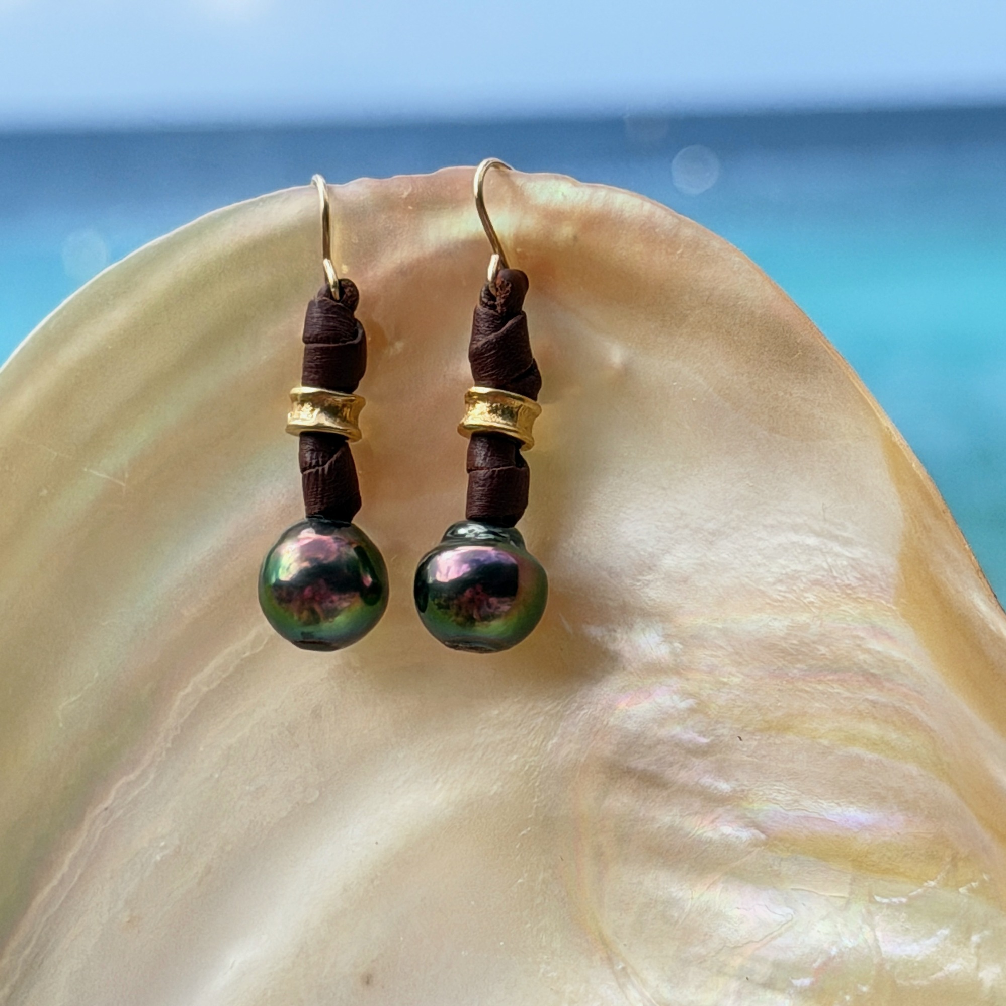 Boucles en cuir, perles vertes de Tahiti et crochets en or, sur un coquillage, détail.