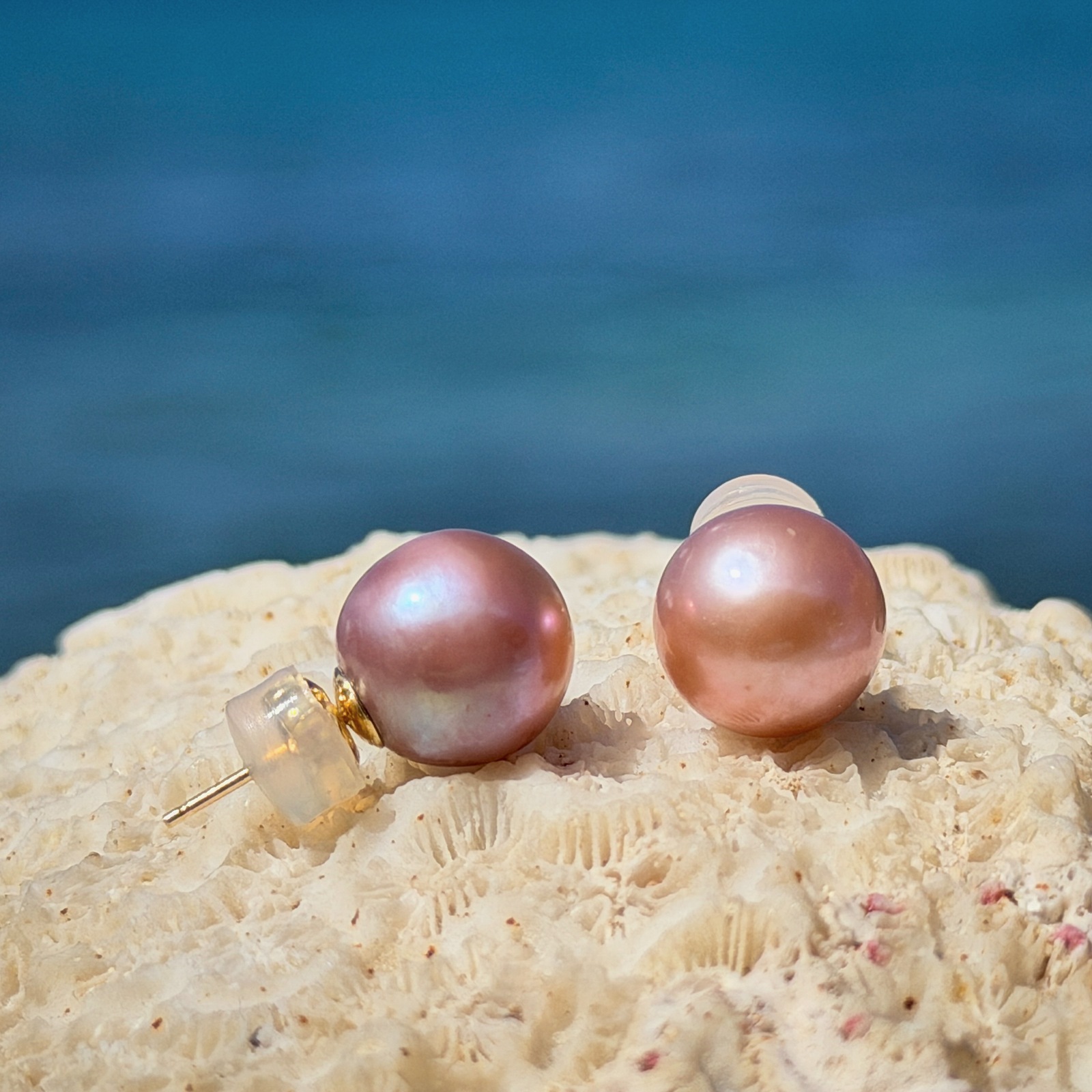 Clous en or et perles roses d’eau douce, montures visibles de côté, sur un support de corail, vue de côté.
