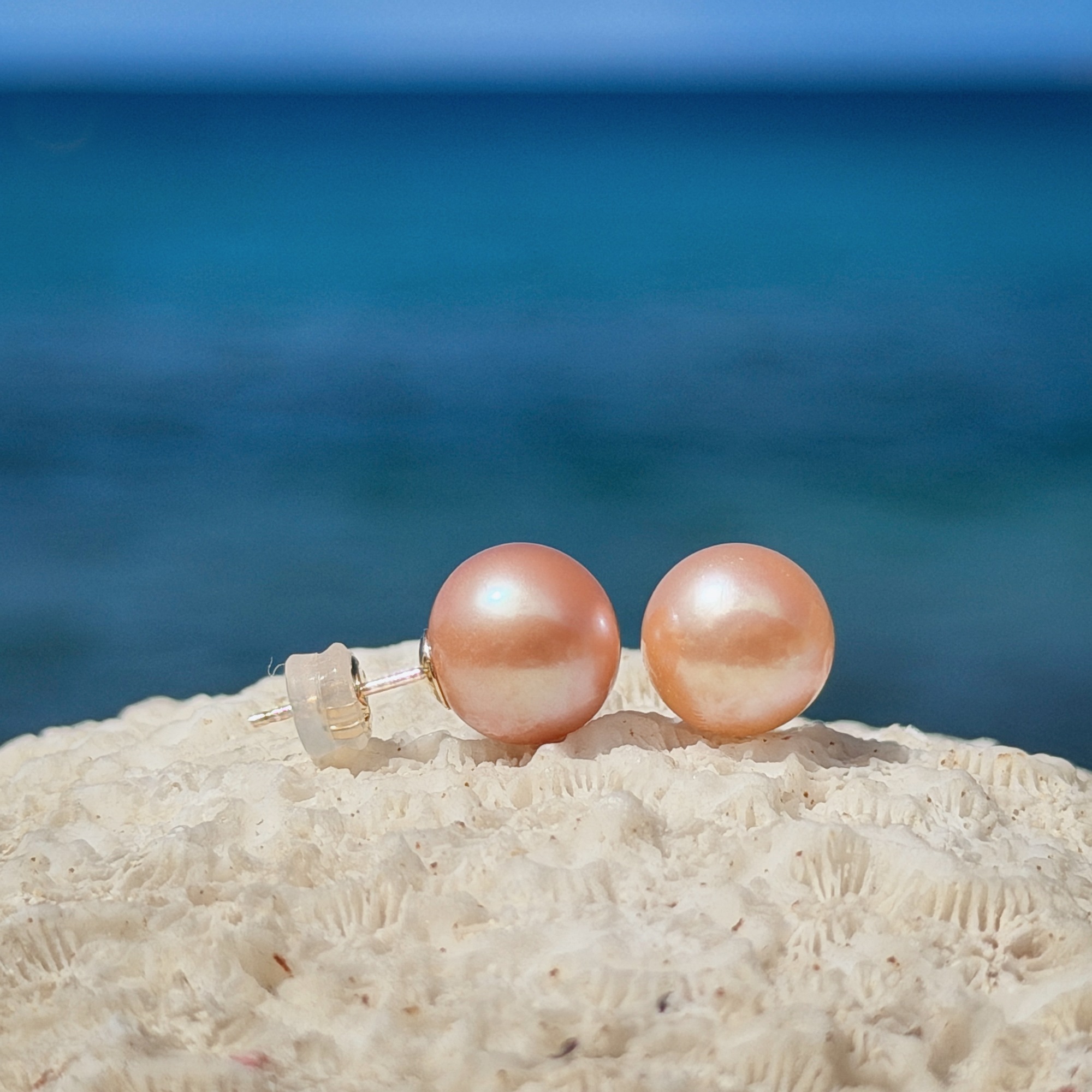 Clous en or et perles roses d’eau douce, perles aux tons pêche, sur un support de corail.
