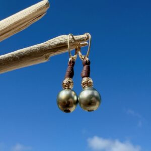 Boucles en cuir, perles de Tahiti et éléments ciselés, sur du bois.