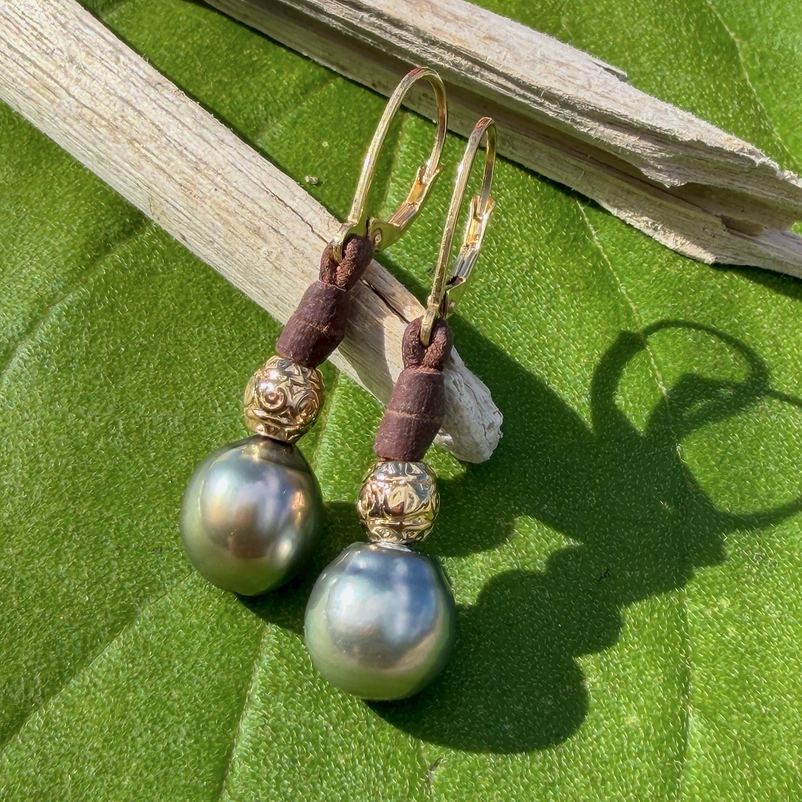 Boucles en cuir, perles de Tahiti et éléments ciselés, sur un feuillage, détail.