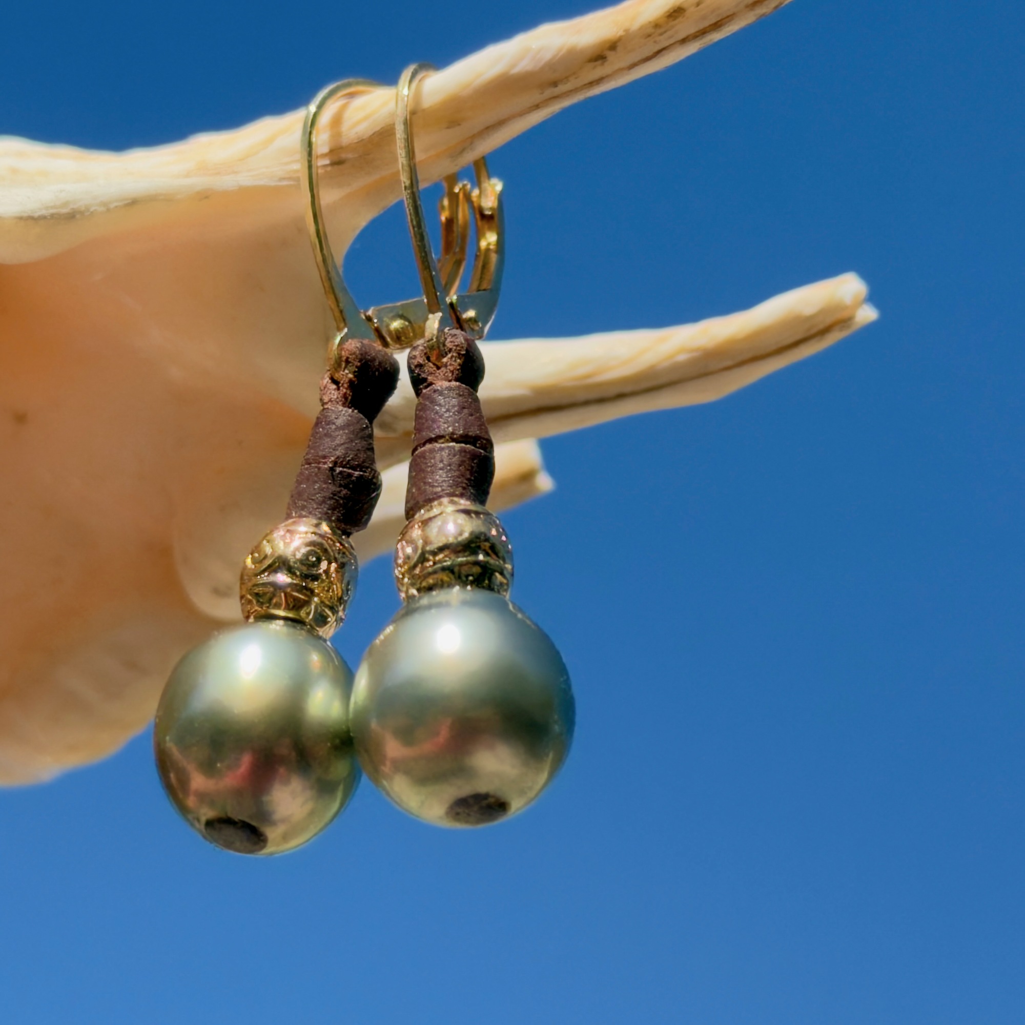 Boucles en cuir, perles de Tahiti et éléments ciselés, sur un coquillage, détail.
