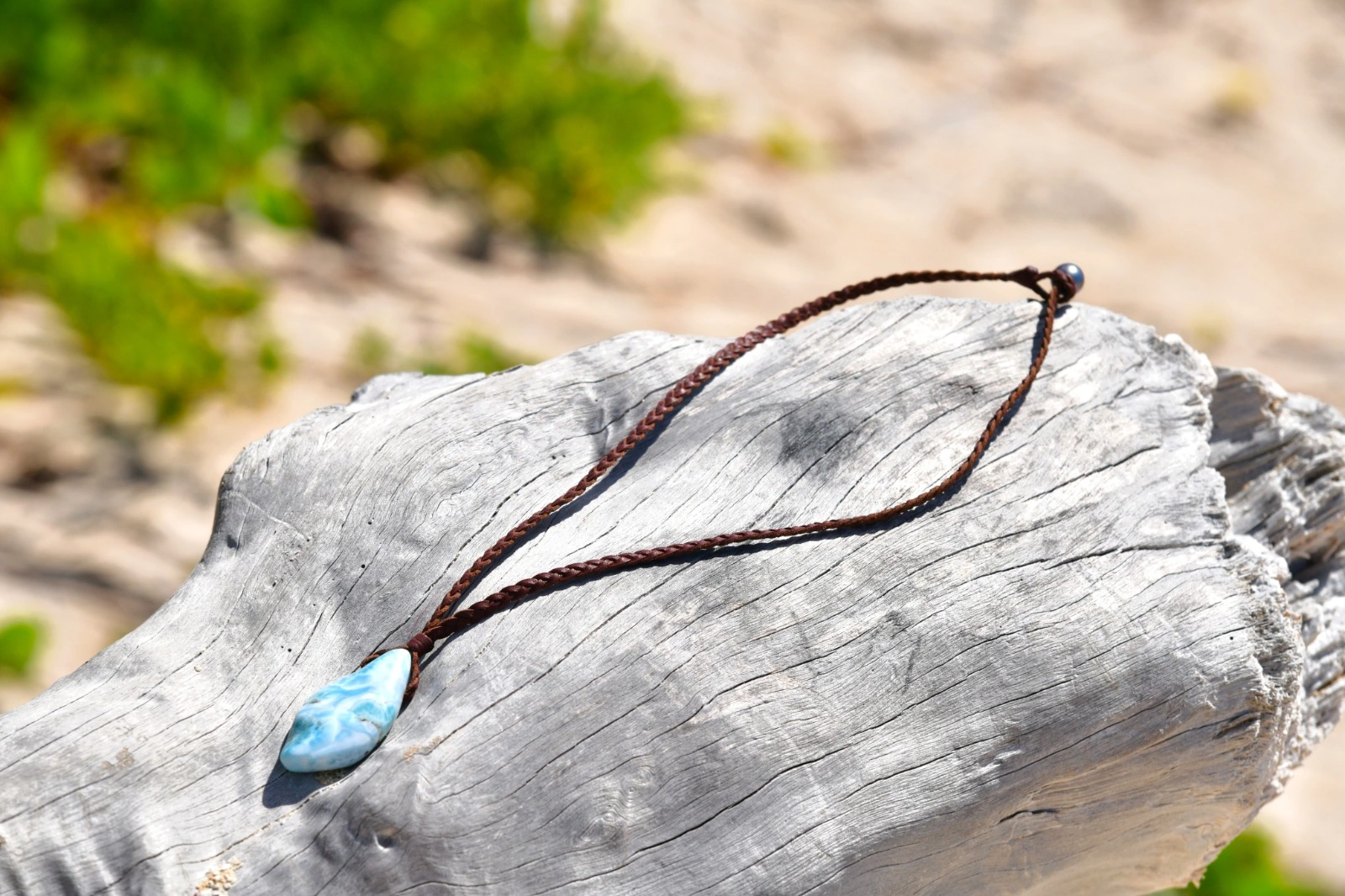 Braided leather necklace with a Larimar pendant arranged on driftwood