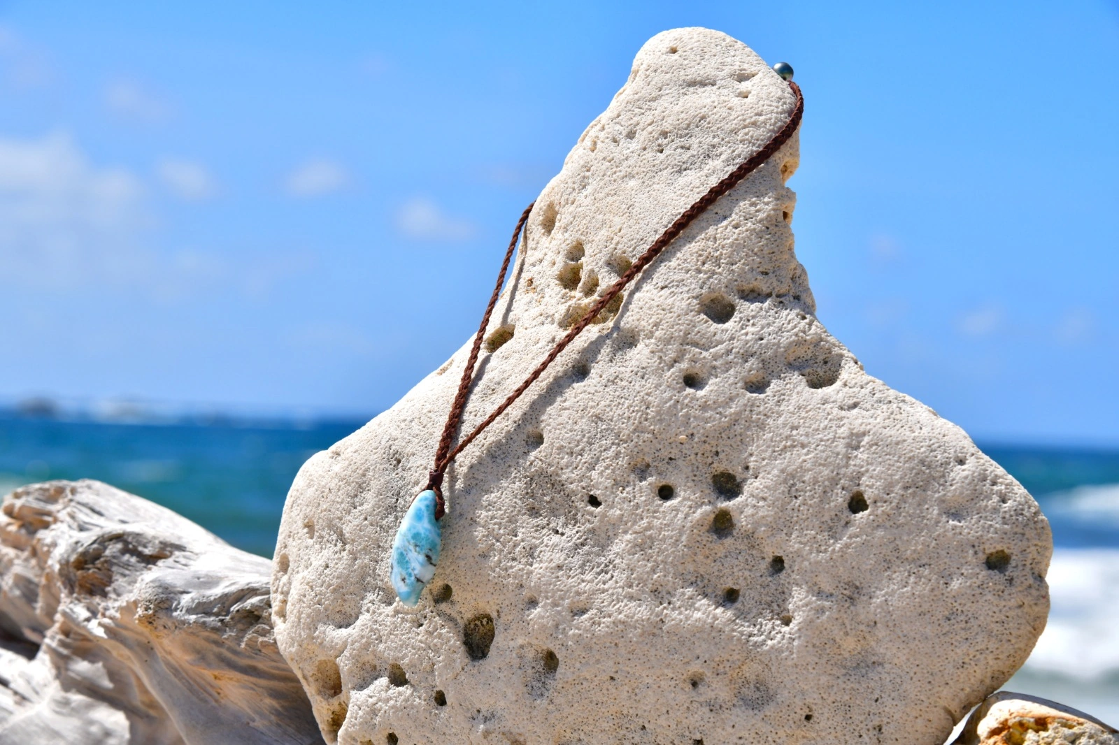 Full view of a braided kangaroo leather necklace with a Larimar pendant displayed on a rock by the sea