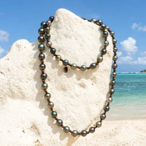 Vue d’ensemble du sautoir en cuir avec 68 perles de culture de Tahiti présenté sur un support corallien à la plage