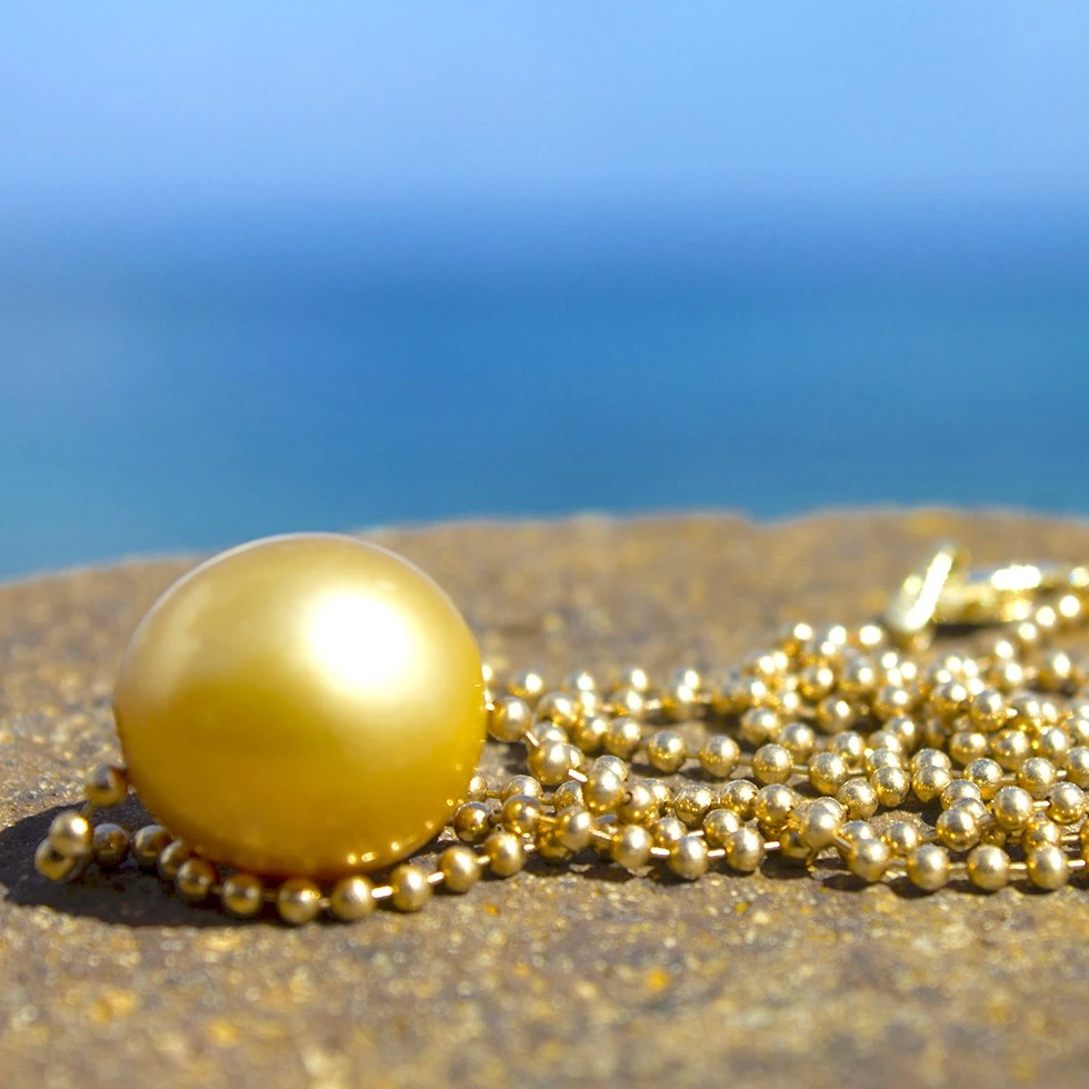 14-karat gold chain necklace with its 12 mm golden South Sea pearl and clasp grouped on a rock facing the sea