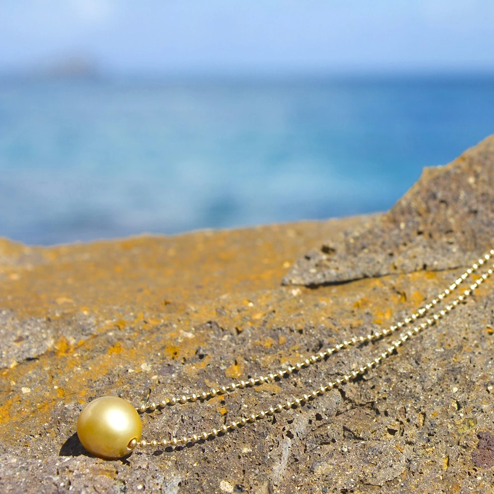 14-karat gold chain necklace with a 12 mm golden South Sea pearl laid out on a rock facing the sea