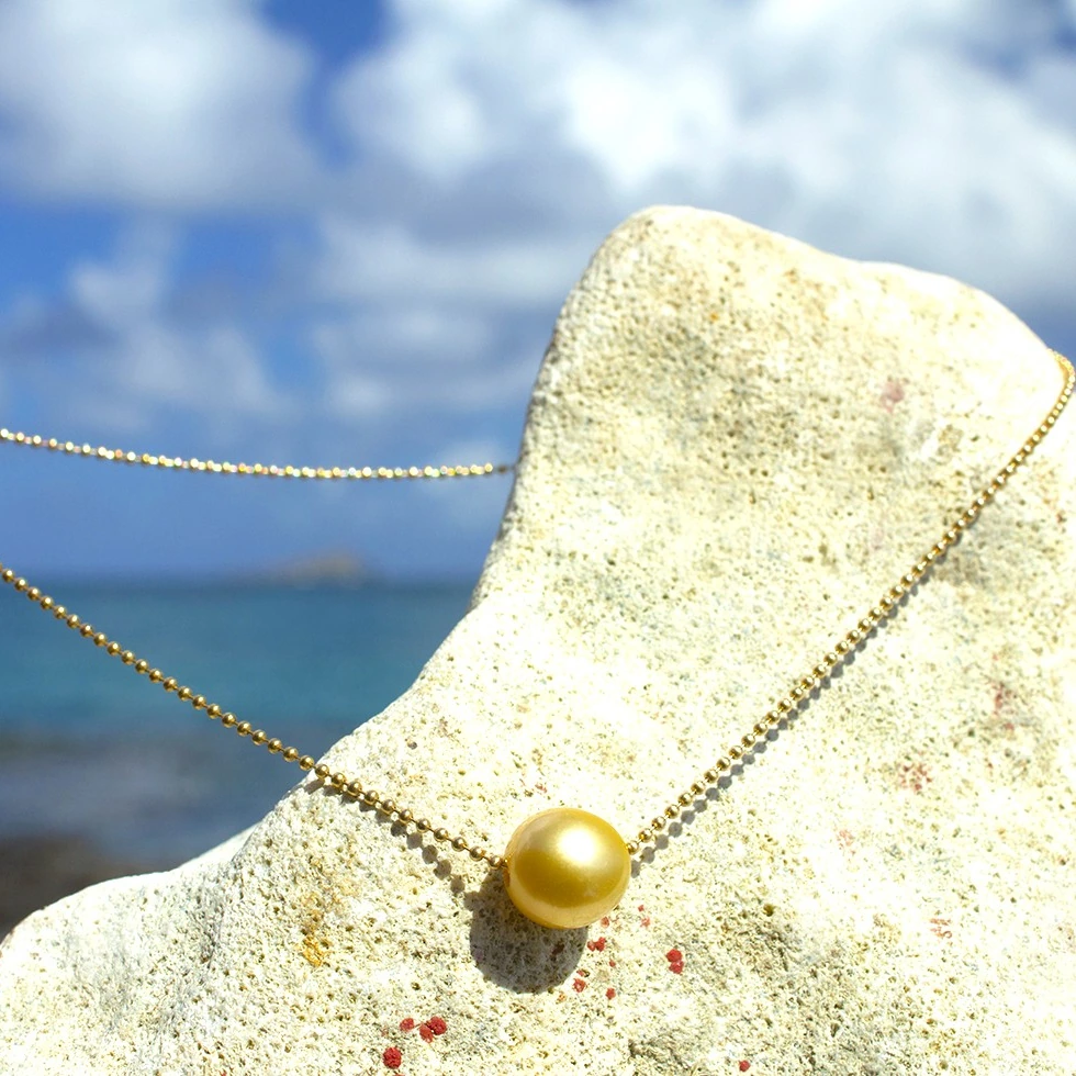 14-karat gold chain choker necklace with a 12 mm golden South Sea pearl displayed on a coral stand facing the sea
