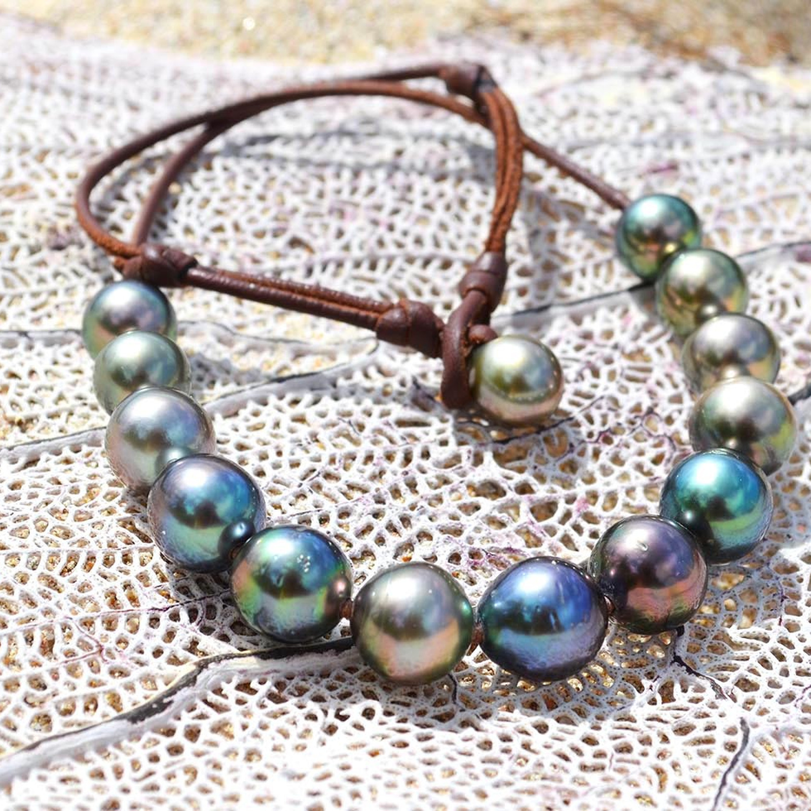 Adjustable brown leather choker with 14 multicolored Tahitian cultured pearls laid out on coral