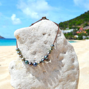 Collier ras du cou ajustable en cuir marron avec 14 perles de culture de Tahiti multicolores présenté sur un rocher à la plage