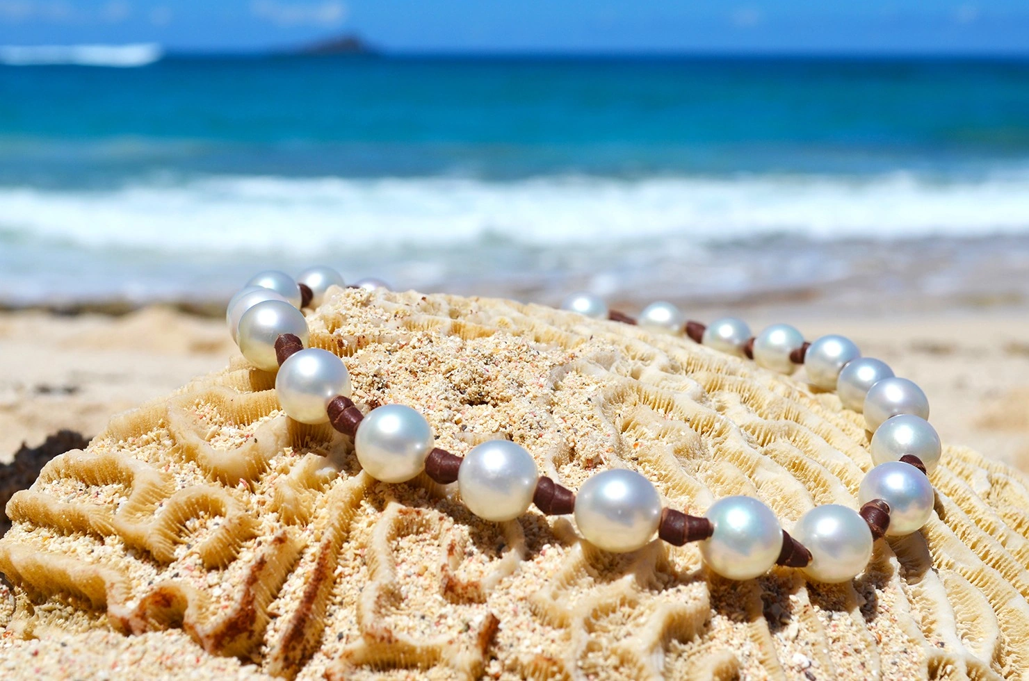 Vue rapprochée du collier ras du cou avec 23 perles blanches des mers du Sud présenté sur du corail à la plage