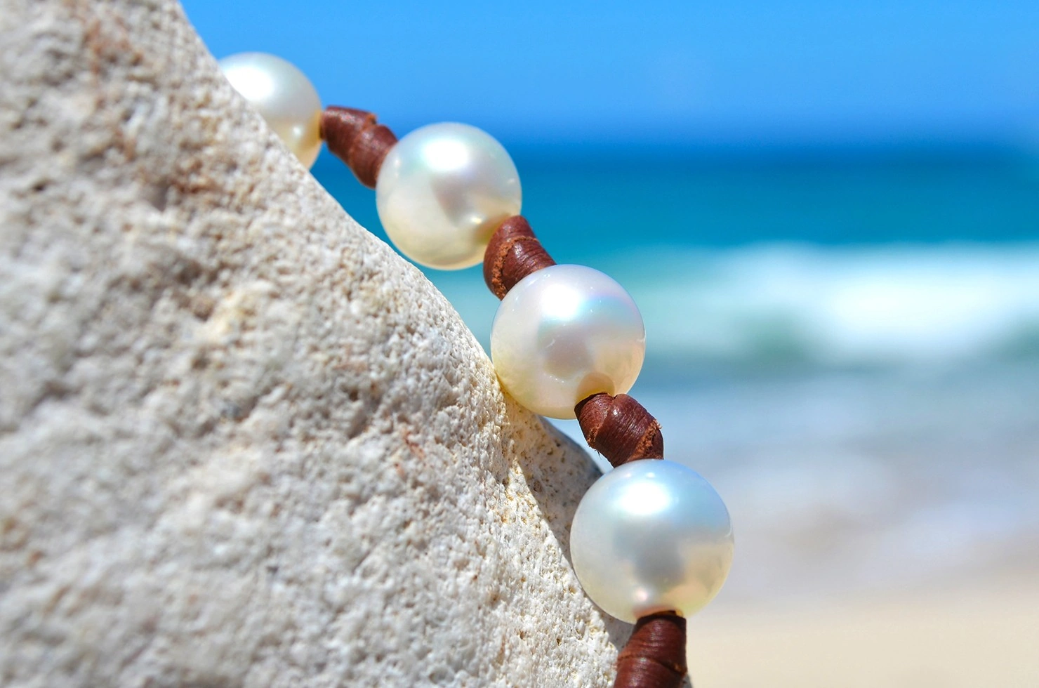 Gros plan sur les perles blanches des mers du Sud et les nœuds en cuir marron du collier ras du cou face à la mer