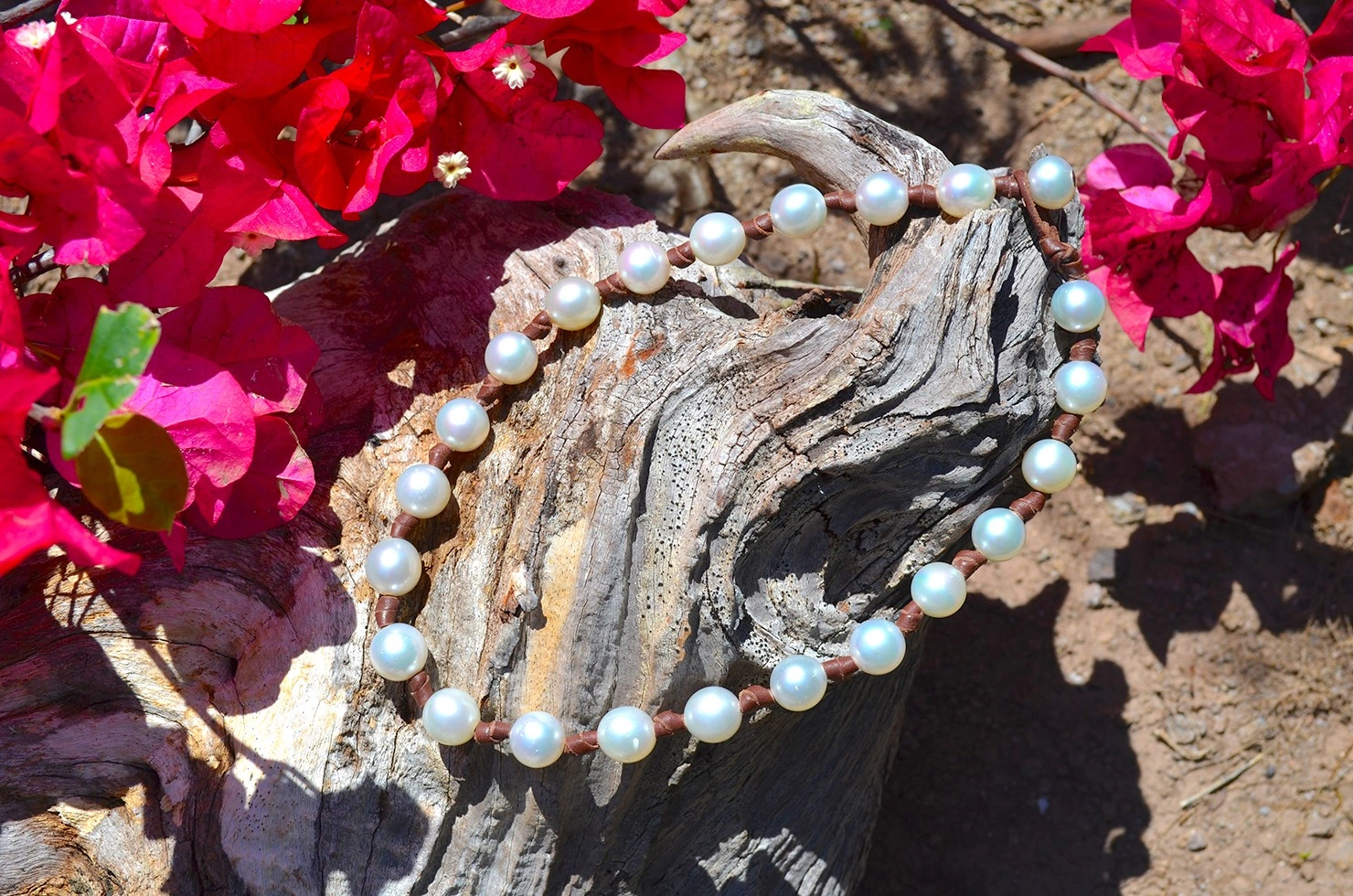 Collier ras du cou avec 23 perles blanches des mers du Sud disposé sur du bois parmi des fleurs roses