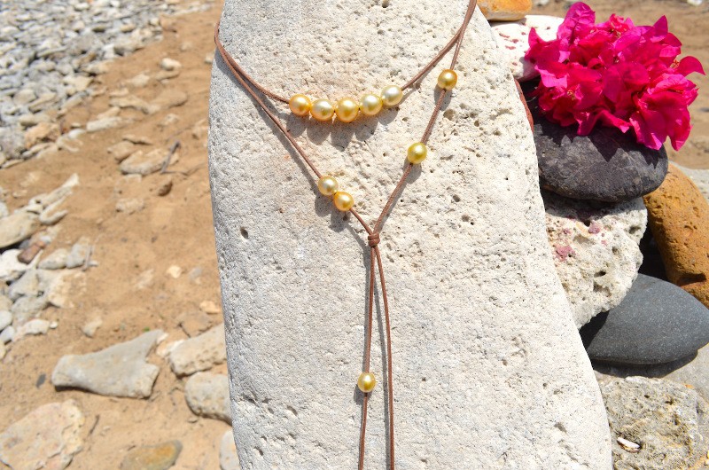 Vue complète du sautoir ajustable en cuir avec 12 perles dorées des mers du Sud présenté sur une roche