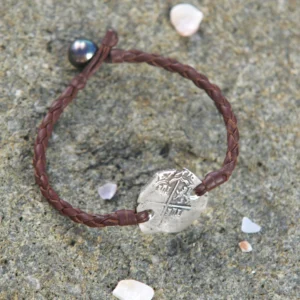 Bracelet en cuir tressé avec monnaie ancienne en argent et perle de Tahiti présenté sur un rocher