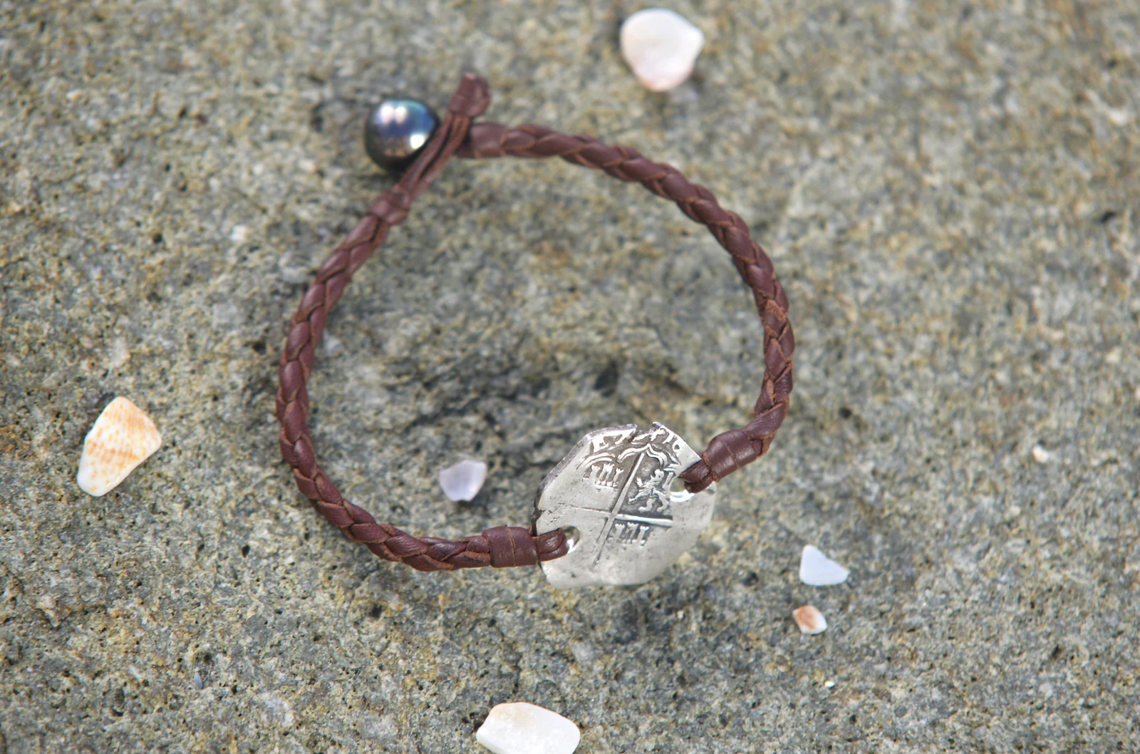 Bracelet en cuir tressé avec monnaie ancienne en argent et perle de Tahiti présenté sur un rocher