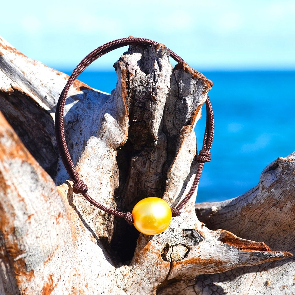 Vue d’ensemble du bracelet ajustable avec une perle dorée d’Australie de 11,5 mm présenté sur du bois face à la mer