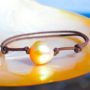 Bracelet ajustable avec une perle dorée d’Australie de 12 mm présenté sur une nacre face à la mer