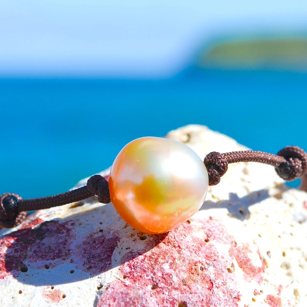 Bracelet ajustable avec une perle dorée d’Australie de 12 mm présenté sur une roche face à la mer