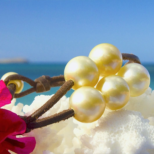 Full view of the leather bracelet with five golden Australian pearls displayed on white coral by the sea