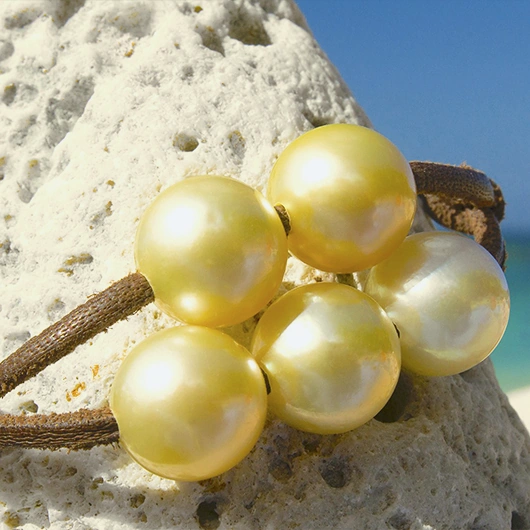 Detail of the five golden Australian pearls on the leather bracelet displayed on a rock by the sea