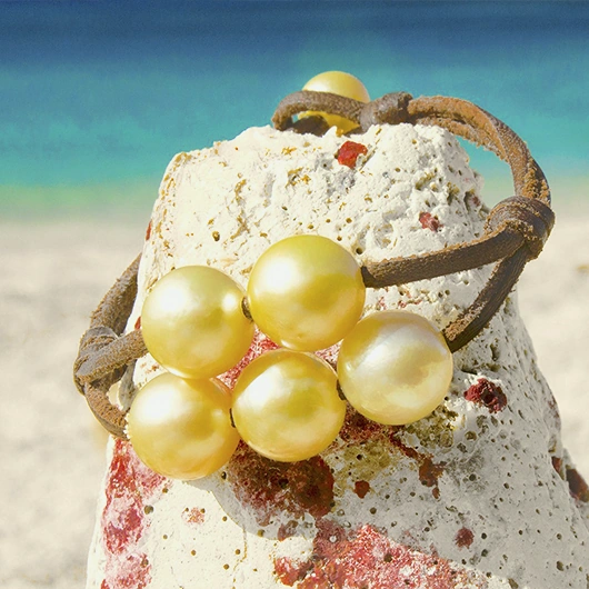 Leather bracelet with five golden Australian pearls displayed on a rock by the sea