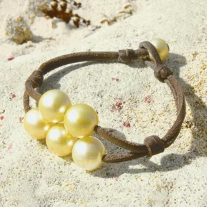 Brown leather bracelet with five golden Australian cultured pearls displayed on sand
