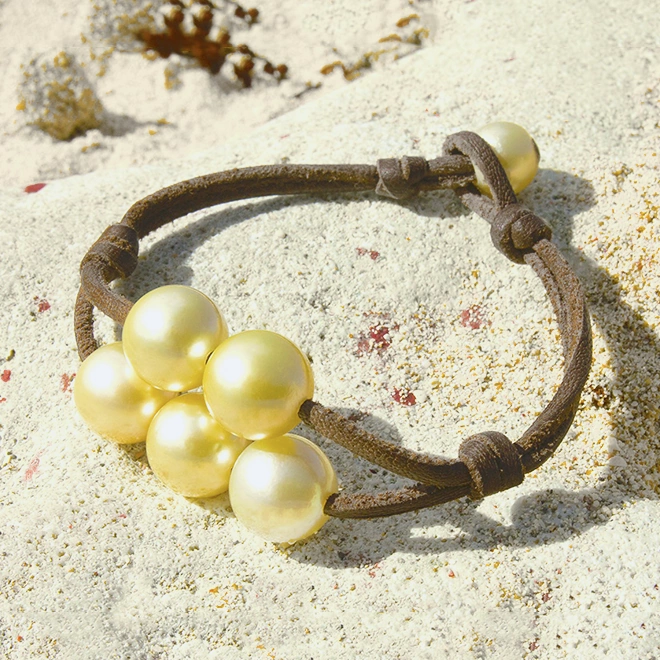 Brown leather bracelet with five golden Australian cultured pearls displayed on sand