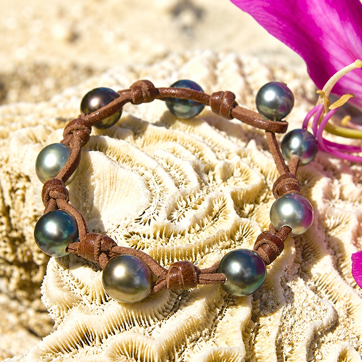 Full view of the leather bracelet with nine multicolored Tahitian pearls and knots displayed on a shell with pink flowers