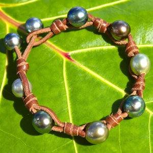 Leather bracelet with nine multicolored Tahitian pearls and knots displayed on a green leaf