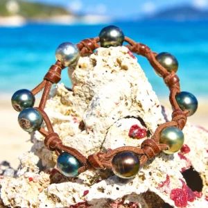 Leather bracelet with nine multicolored Tahitian pearls and knots displayed on a rock by the sea