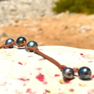 Leather bracelet with three 9.5 mm Tahitian pearls and knots displayed on a rock at the beach