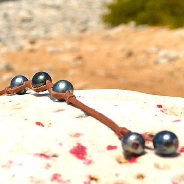 Bracelet en cuir avec trois perles de Tahiti de 9,5 mm et des nœuds présenté sur une roche à la plage