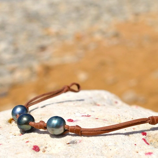 Bracelet avec trois perles de Tahiti de 9,5 mm, des nœuds et deux perles de fermeture présenté sur une roche au bord de mer