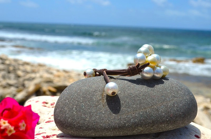 Détail du montage en cuir et des perles de fermeture du bracelet à trois rangs présenté sur une roche face à la mer