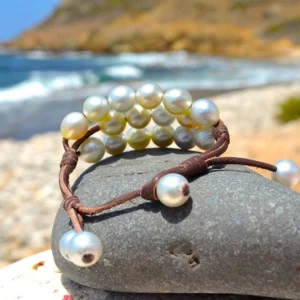 Three-strand bracelet with twenty white Australian pearls displayed on a rock by the sea