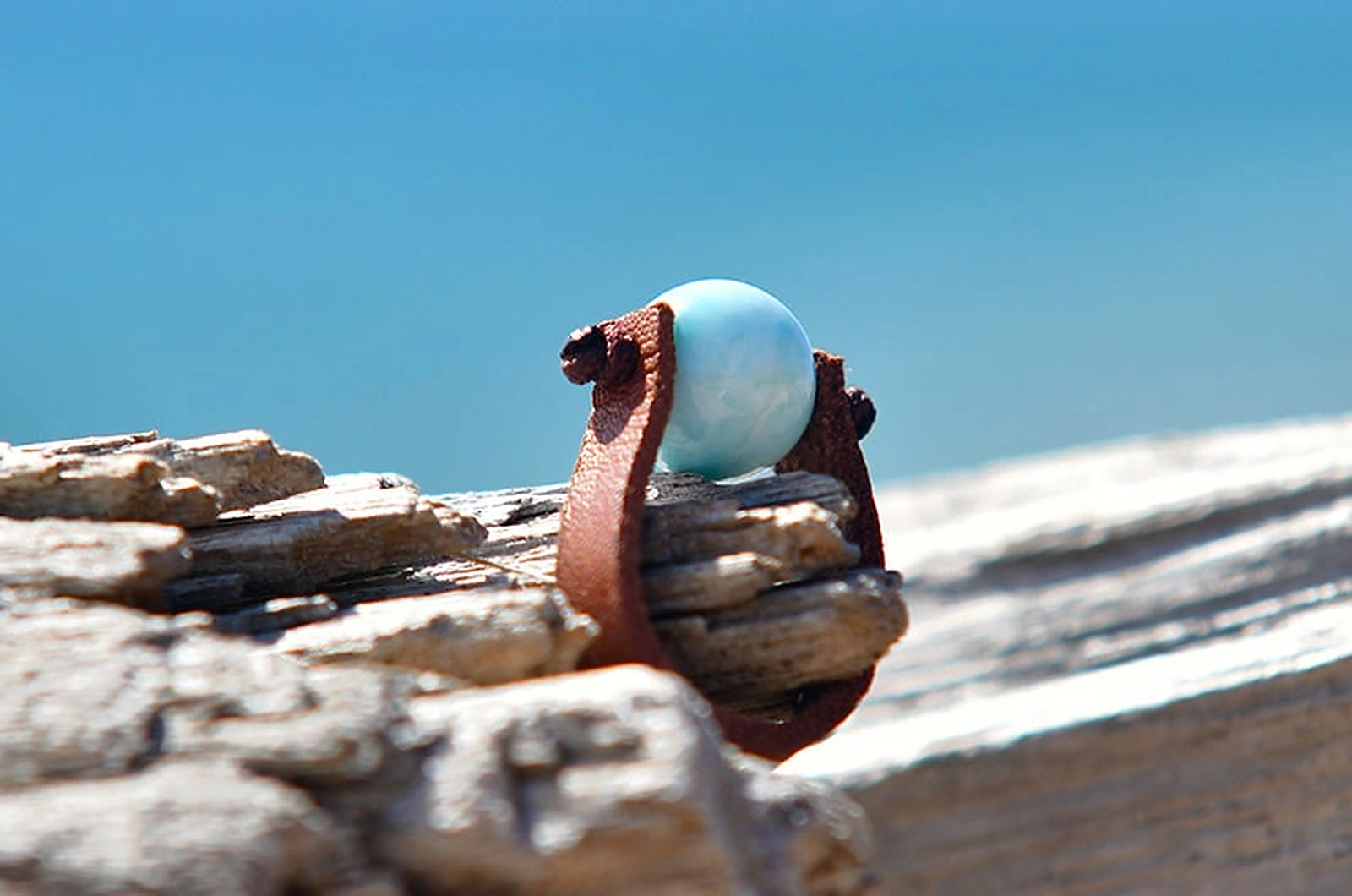 Side view of the brown leather ring with a round 10 mm Larimar displayed on driftwood