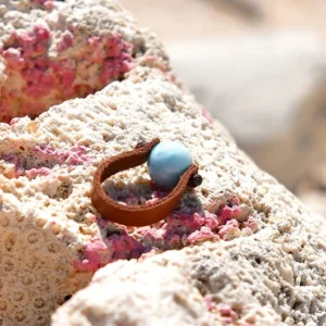 Bague en cuir marron avec Larimar rond de 10 mm présentée sur du corail