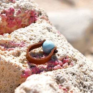 Bague en cuir marron avec Larimar rond de 10 mm présentée sur du corail