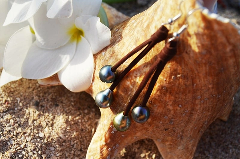 Leather drop earrings with four Tahitian pearls displayed on wood with white flowers