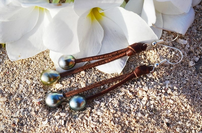 Leather drop earrings with four Tahitian pearls displayed on coral with white flowers