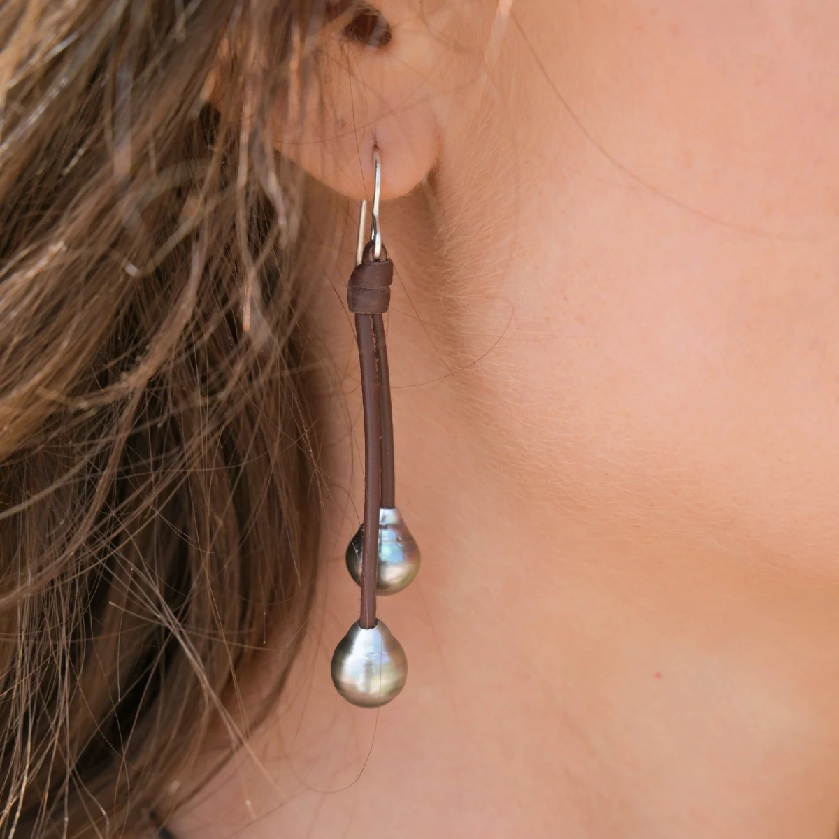Close-up of leather drop earrings with four Tahitian pearls being worn