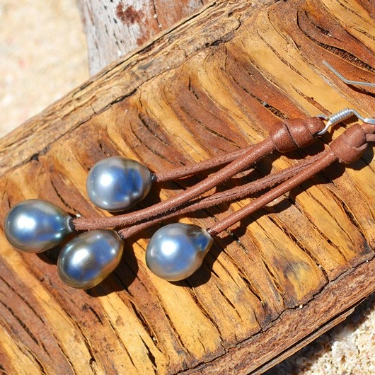 Brown leather drop earrings with four Tahitian pearls displayed on wood
