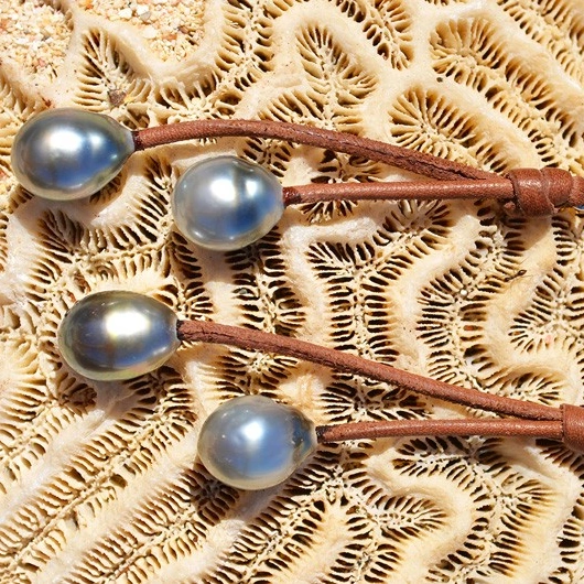 Brown leather drop earrings with four Tahitian pearls displayed on coral